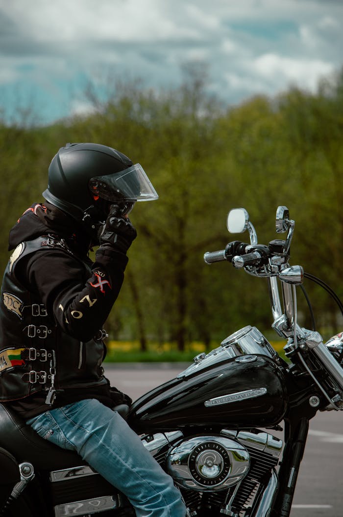 A biker adjusting helmet on a Harley Davidson motorcycle parked outdoors in Lithuania.