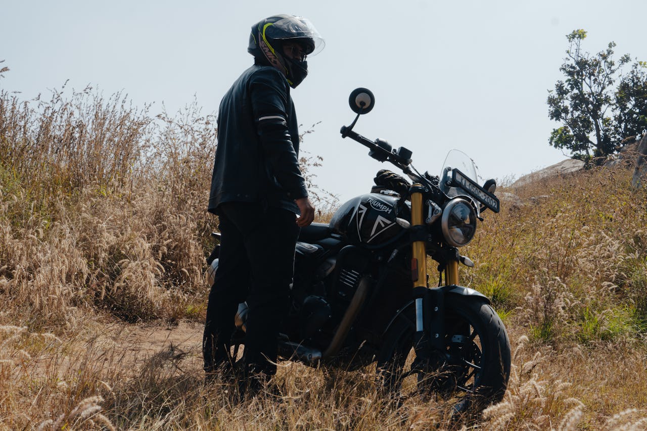 A motorcyclist stands with a black motorcycle in Bengaluru's scenic countryside, capturing adventure.